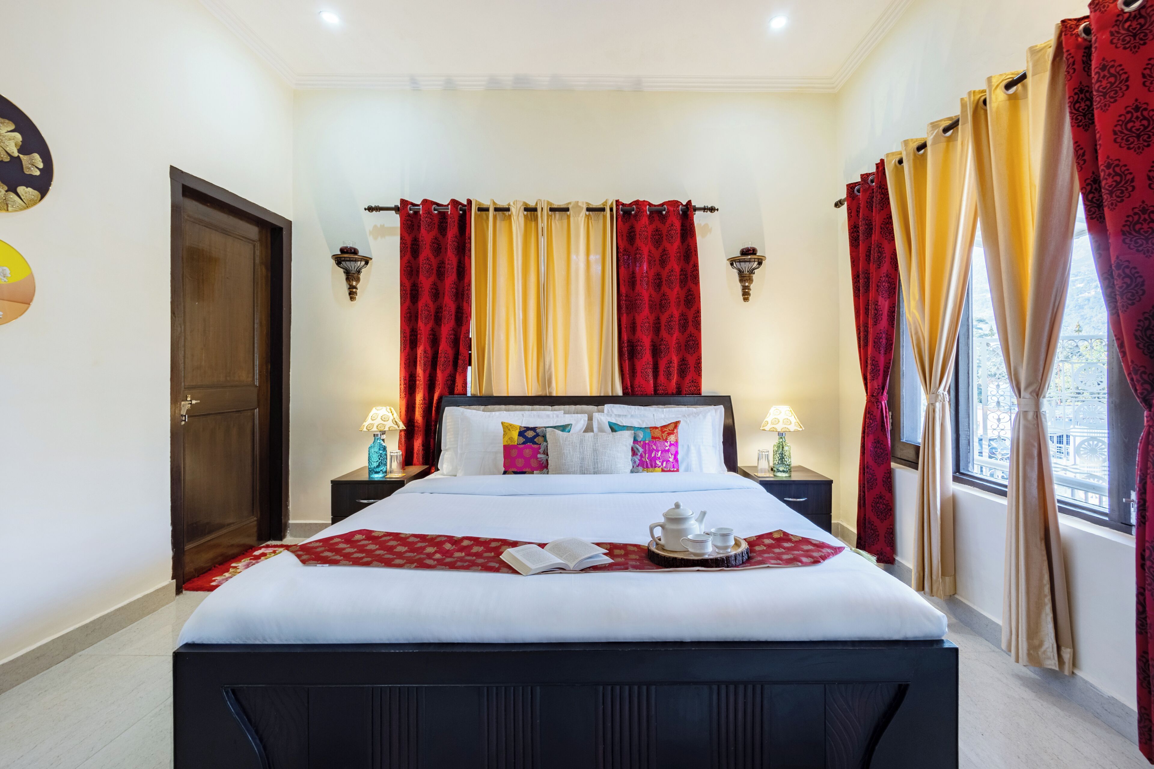 A neatly made bed with pillows, a bedside table with a lamp, and a window with curtains.