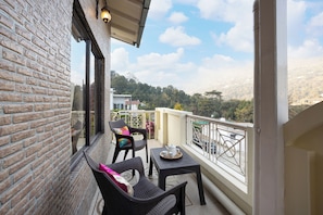 Un balcon agrémenté de meubles en osier, une petite table avec une théière, et une vue sur un paysage montagneux.
