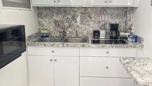 A kitchen with white cabinets, a granite countertop, a microwave, a coffee maker, and a small plant. - 5 minutes from National Forest and 8 of the best beaches / Natural Essence (Luquillo)
