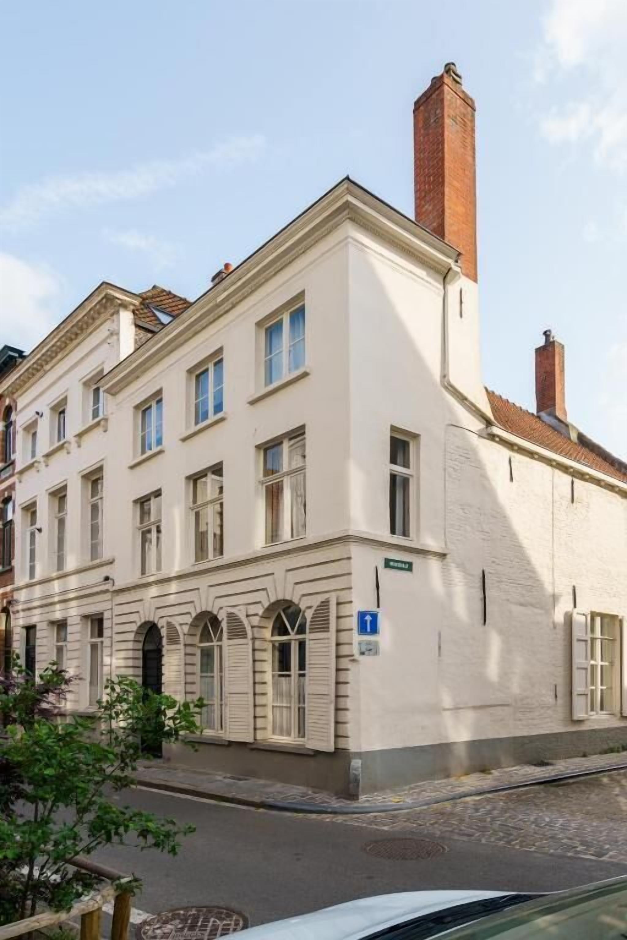 Un edificio de varios pisos con un estilo arquitectónico clásico, que destaca una chimenea y una entrada hacia la calle.