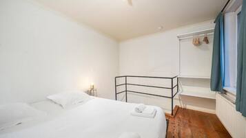 Una habitación con una cama litera, una mesita de noche pequeña con una lámpara y una ventana con cortinas.