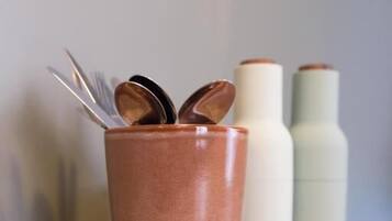 A wooden surface with a copper-colored mug containing spoons and two white bottles with brown caps.