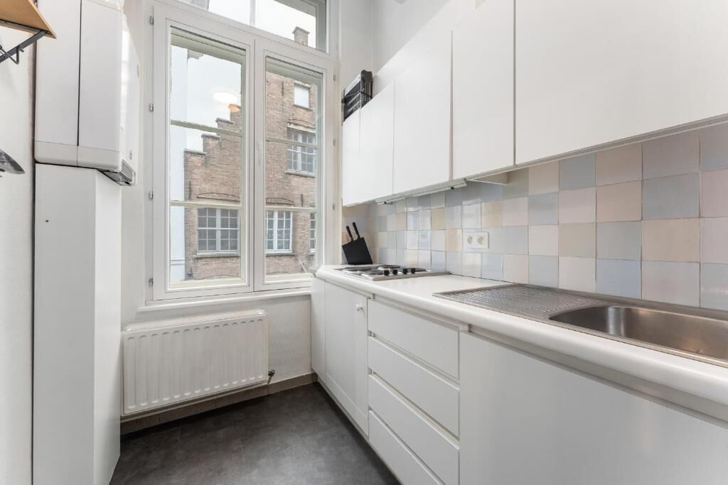 A kitchen with white cabinets, a window, a radiator, and a tiled backsplash.