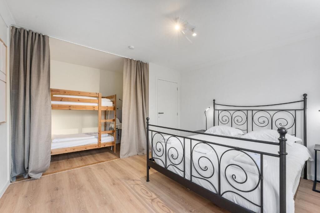 Una habitación con una litera, una cama individual, suelo de madera y una puerta.