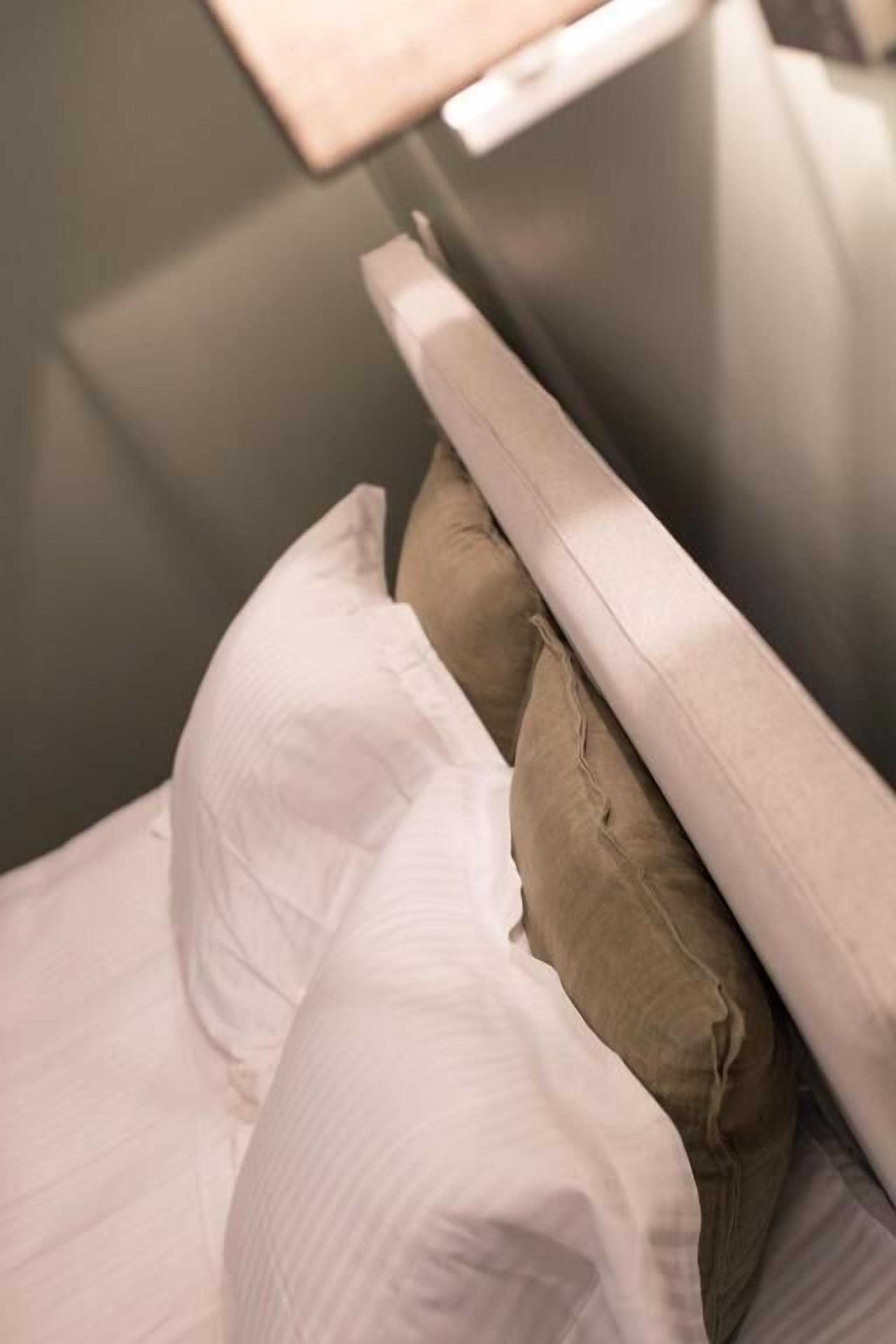 Una cama con almohadas blancas y marrones, cabecera de madera y pared gris.