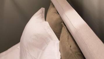 Una cama con almohadas blancas y marrones, cabecera de madera y pared gris.