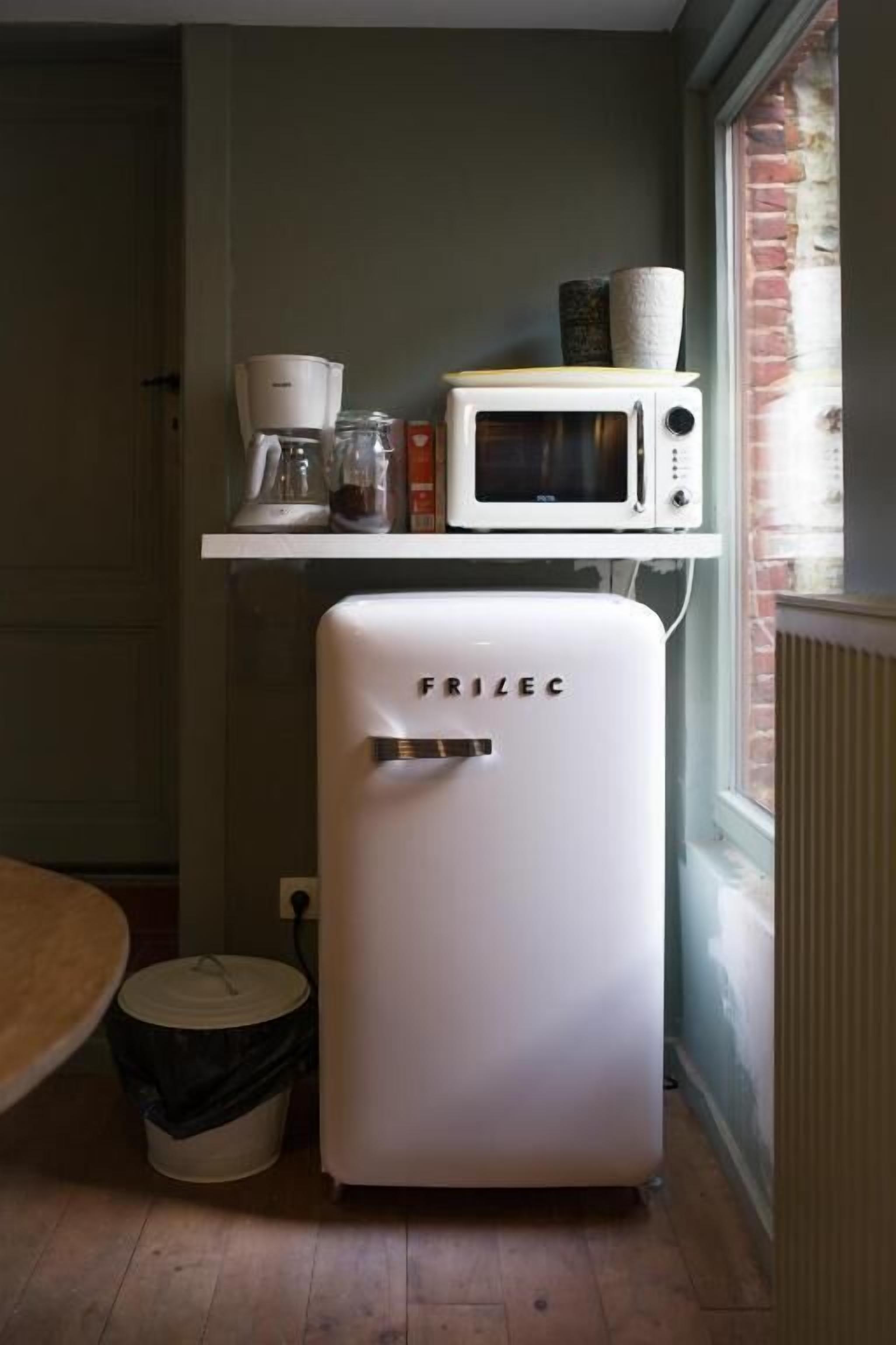 Eine kompakte Küche mit einem weißen Frizlec-Kühlschrank, einer Mikrowelle und einer Kaffeemaschine auf einem Regal.