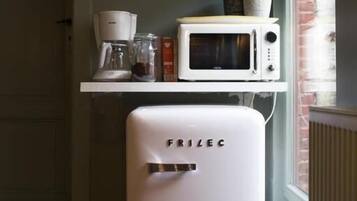 Eine kompakte Küche mit einem weißen Frizlec-Kühlschrank, einer Mikrowelle und einer Kaffeemaschine auf einem Regal.