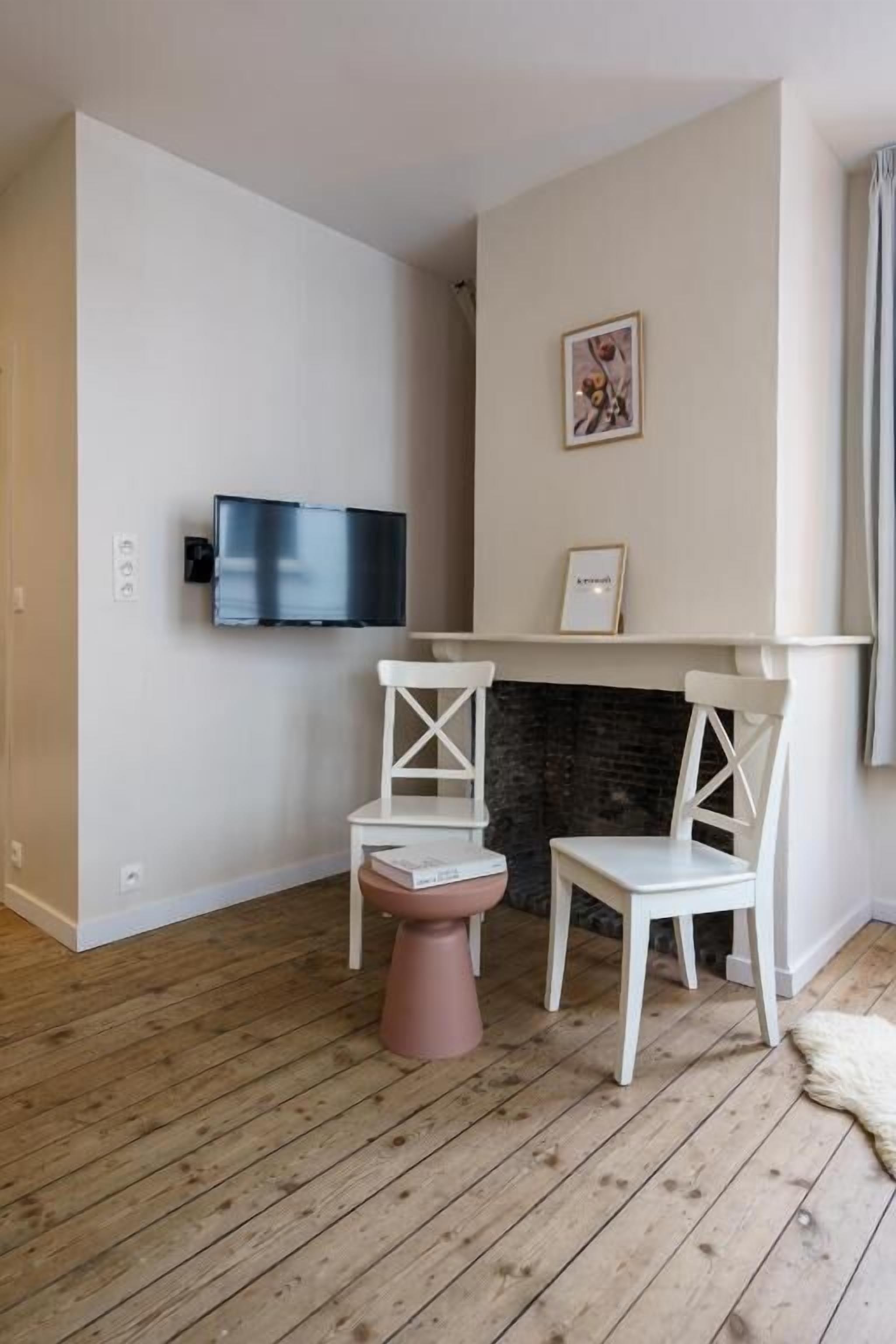 A room with a fireplace, a television mounted on the wall, and two white chairs.