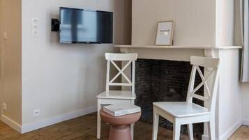 A room with a fireplace, a television mounted on the wall, and two white chairs.