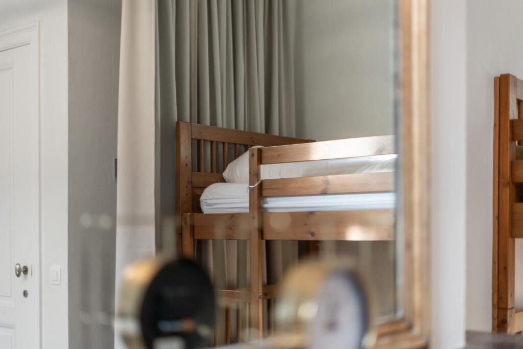 Een houten stapelbed in een kamer met een witte deur en een spiegel die een deel van de kamer weerkaatst.