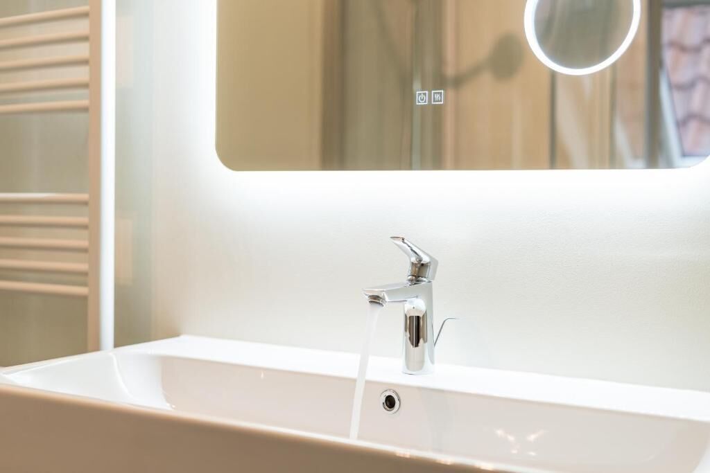 Une salle de bain avec un lavabo blanc, un miroir et un robinet d’où coule de l’eau.