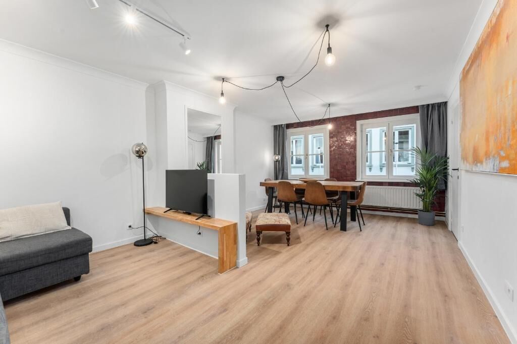 Ein modernes Wohnzimmer mit Sofa, Fernseher, Esstisch, Stühlen und einem großen Fenster.