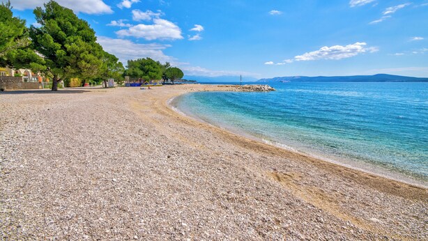 A pebble beach with clear water, trees, and a distant shoreline. - Luxury vacation apartment with whirlpool for 4-6 people in Crikvenica (Crikvenica)