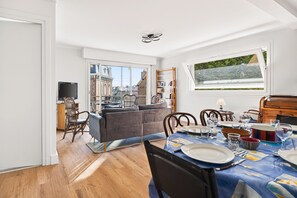 A modern living room with a sofa, dining table set, and a large window with a view. - Stunning sea and beach view for 6 (Dinard)