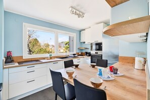 A modern kitchen with white cabinets, a wooden dining table, and a view of the outdoors. - Stunning sea and beach view for 6 (Dinard)