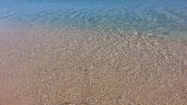 A beach with clear shallow water and a sandy shore.