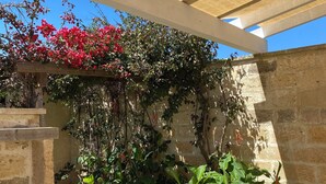A covered outdoor area with a pergola, stone walls, and various plants.