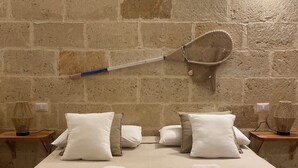 A neatly made bed with white linens and towels, a wall-mounted badminton racket, and two bedside tables with decorative items.