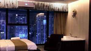 A hotel room with a bed, a chair, a bathtub, and a large window with a city view. - Namaste B&B With Jacuzzi I Noida (Greater Noida)