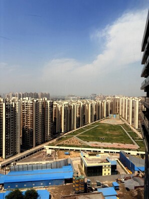 A high-rise residential area with multiple apartment buildings, a sports field, and industrial buildings with blue roofs. - Namaste B&B With Jacuzzi I Noida (Greater Noida)