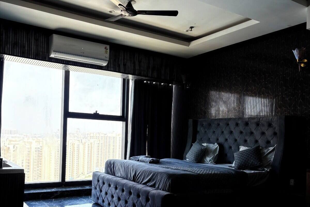 Un dormitorio con cama, ventilador de techo, ventana grande y vista a la ciudad.