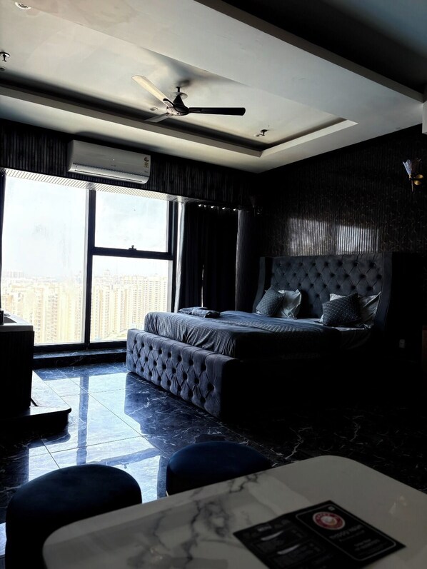 A bedroom with a bed, a ceiling fan, a large window, and a view of the city. - Namaste B&B With Jacuzzi I Noida (Greater Noida)