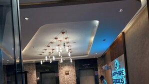 A modern lobby with a reception desk, elevators, and a sign for 'Sapphire Studios'. - Namaste B&B With Jacuzzi I Noida (Greater Noida)