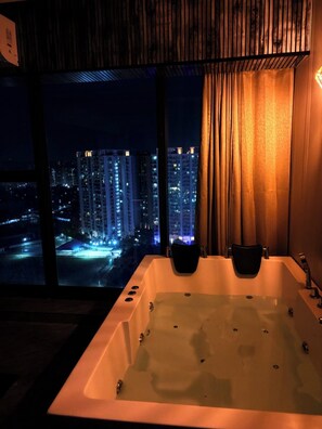 A modern bathroom with a large bathtub, a view of a cityscape at night, and a curtain. - Namaste B&B With Jacuzzi I Noida (Greater Noida)