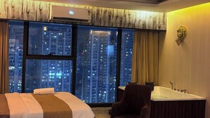 A hotel room with a bed, a chair, a bathtub, and a large window with a city view. - Namaste B&B With Jacuzzi I Noida (Greater Noida)