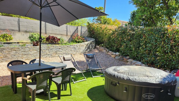 A patio with a table and chairs, a large umbrella, and a hot tub.