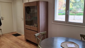 A room with a wooden cabinet, a dining table, and a window with a view of greenery.