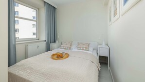 Et soveværelse med seng, vindue, et natbord og en bakke med bagværk.