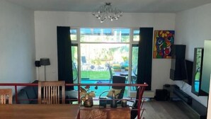A spacious living area with a dining table, chairs, a TV, and a view of the outdoors. - Charming Rooms with free parking (Amsterdam)