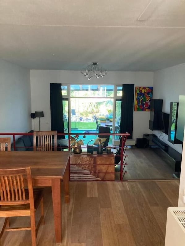 A spacious living area with a dining table, chairs, a TV, and a view of the outdoors.