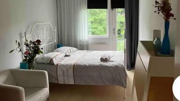 A bedroom with a bed, a chair, a vase with flowers, and a view of greenery outside. - Charming Rooms with free parking (Amsterdam)