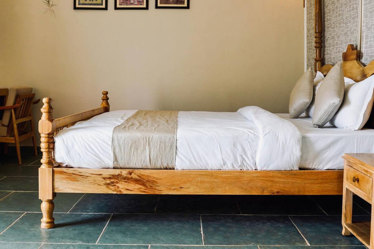 A wooden bed with white bedding, a chair, and three framed pictures on the wall.