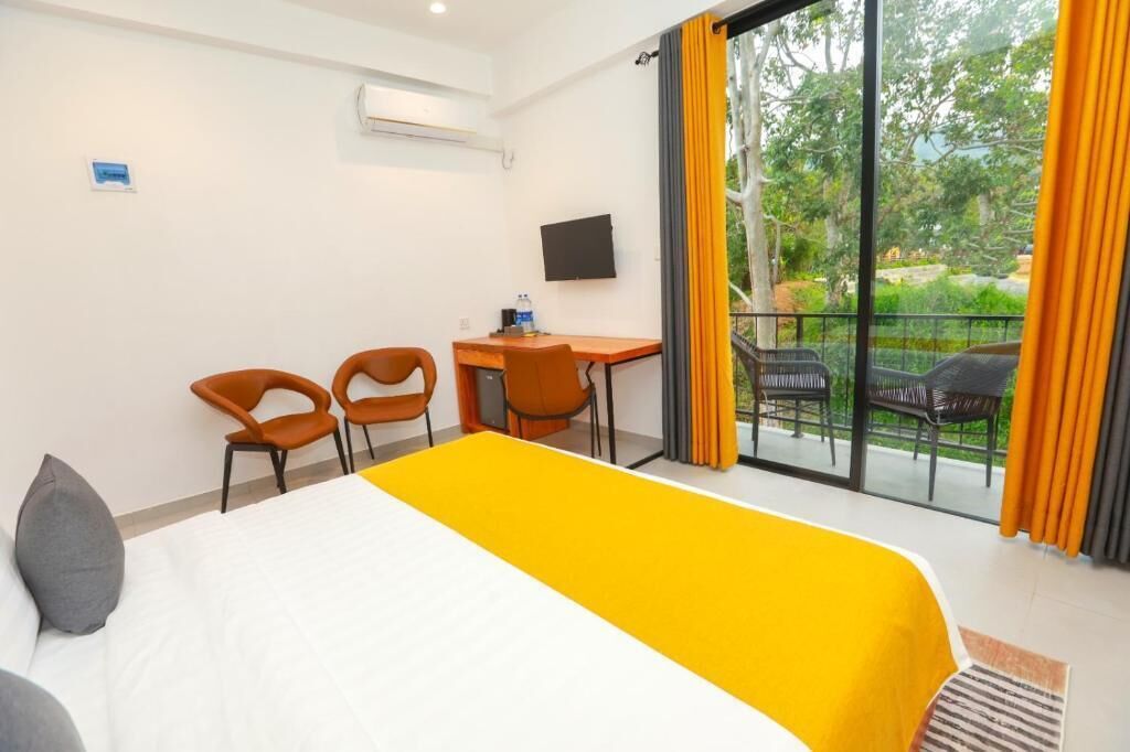 Ein Hotelzimmer mit Bett, zwei Sesseln, einem Schreibtisch, einem Flachbildfernseher und einem Balkon mit Sitzgelegenheit.