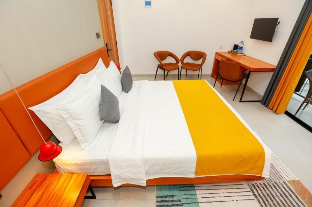 Ein Hotelzimmer mit Bett, Schreibtisch, zwei Stühlen und einem Fernseher an der Wand.