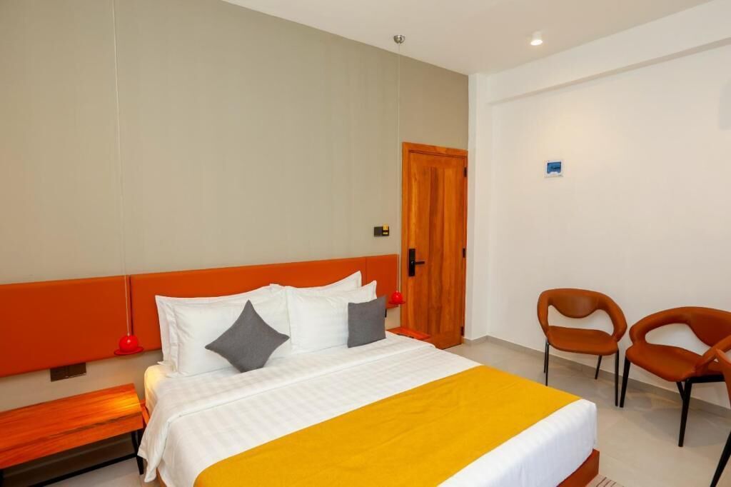 Una camera d'albergo con un letto, una panca, due sedie e una porta.