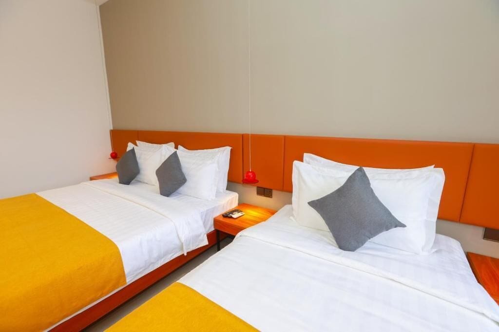 A hotel room with two beds, each with white bedding and orange headboards.