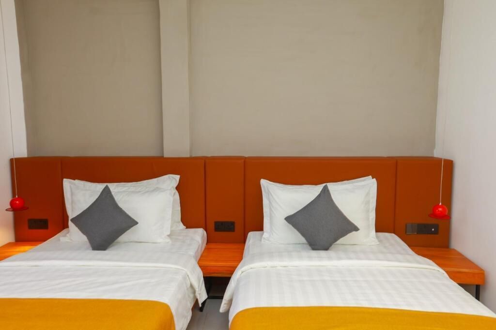 Habitación de hotel con dos camas, cada una con un almohadón y una lámpara colgante roja.