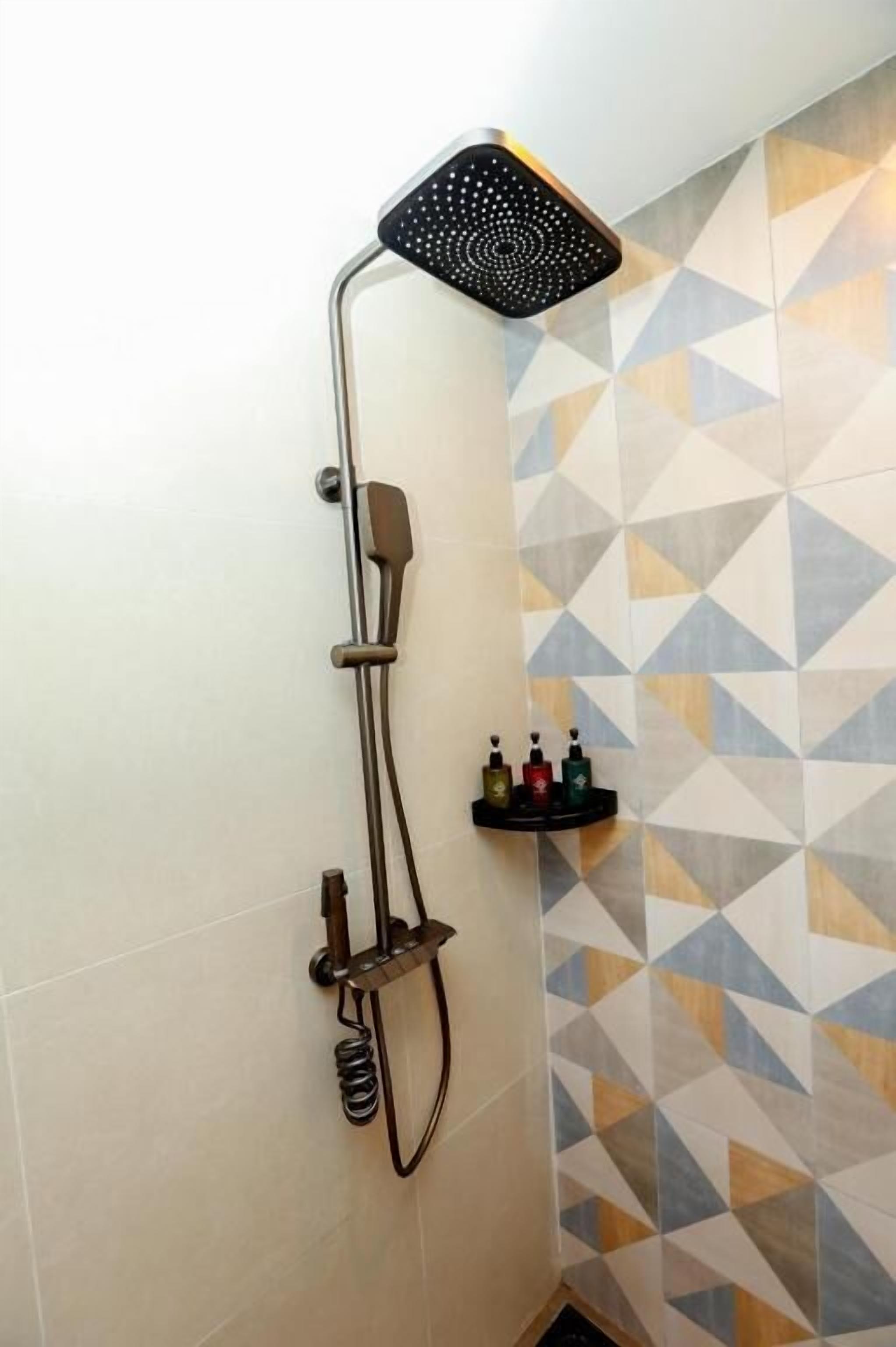 A shower with a handheld head, a wall-mounted control, and a wall-mounted shelf with toiletries.