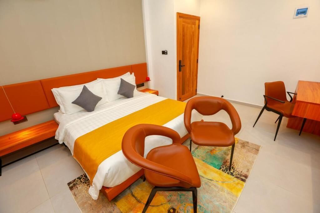 Ein Hotelzimmer mit einem Bett, zwei Stühlen, einem kleinen Tisch, einer Tür und einem Nachttisch.