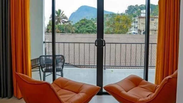 A hotel room with a balcony, two orange chairs, a bed, and a view of a mountain. - Sun Top Grand (Ella)