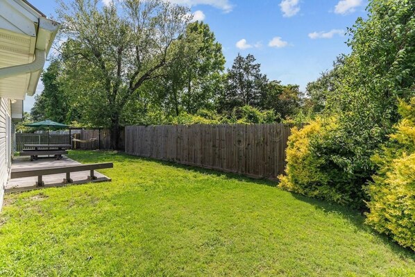 A backyard with a wooden fence, a grassy lawn, and a wooden deck with a bench.