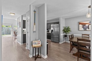 A modern kitchen with stainless steel appliances, a dining area with wooden furniture, and a hallway with a welcome sign.