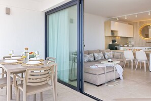 A modern living room with a sofa, a dining table with chairs, a kitchen area, and a sliding glass door leading to a balcony. - 1.6 Amapola Moon - beachfront comfort. (Maspalomas)