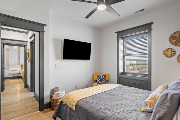 Ein Schlafzimmer mit einem Bett, einem Fernseher, einem Fenster mit Jalousien und einem Deckenventilator.