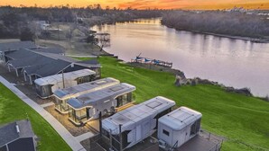 A modern RV park with multiple RVs, a covered picnic area, and a view of a river at sunset. - One-of-a-kind tiny home designed for an unforgettable stay by the beautiful San Jacinto River (Highlands)